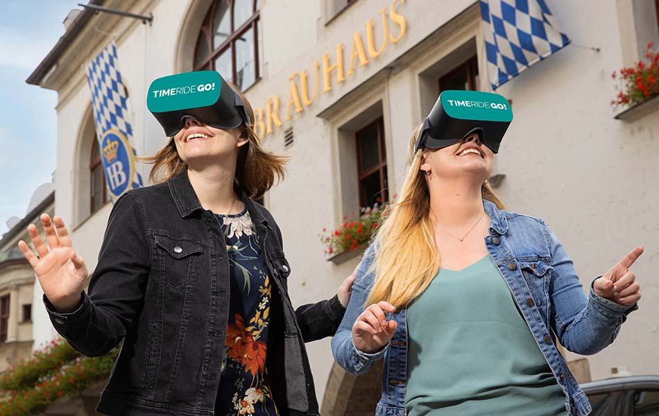 Zwei Damen stehen vorm Hofbraeu Muenchen und erleben eine Virtual Reality Tour.