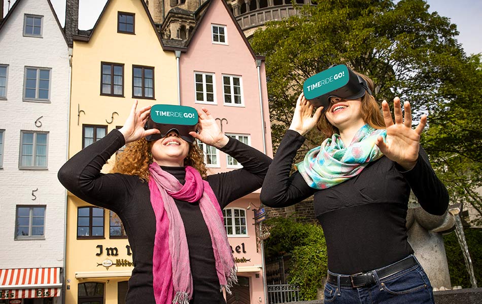 Zwei Frauen erleben mit VR-Brillen eine Zeitreise in der Kölner Altstadt.